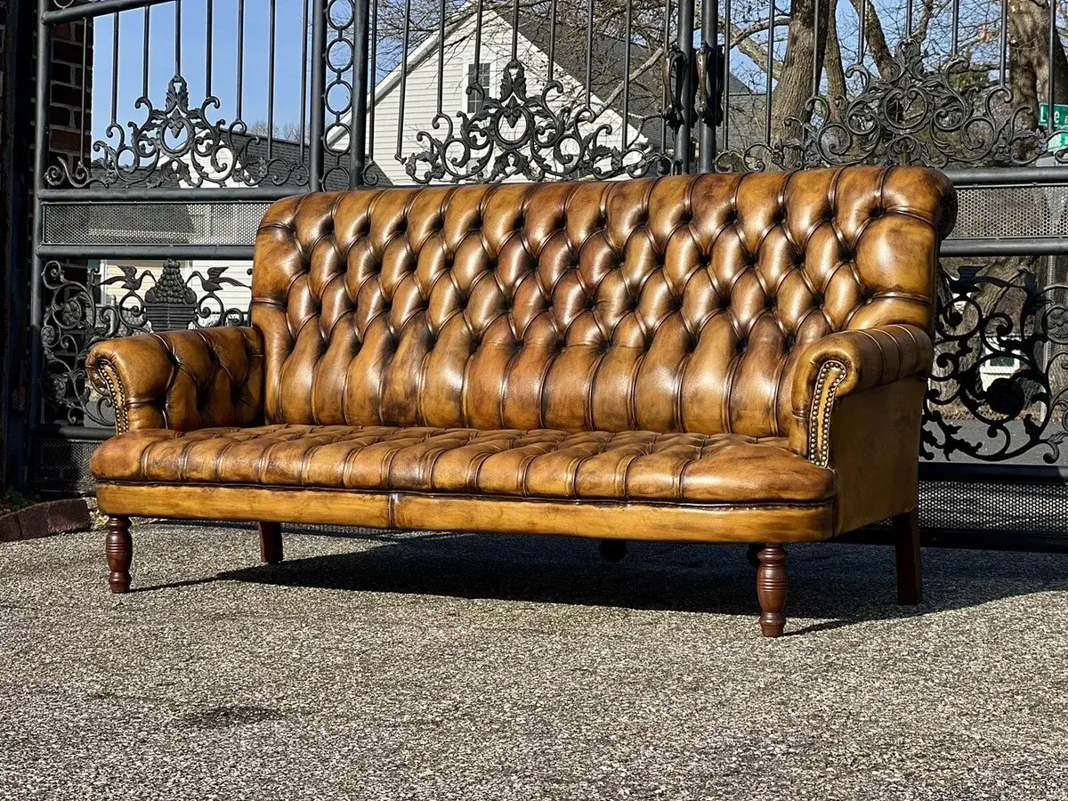 Brązowa, pikowana kanapa skórzana Chesterfield. Dlaczego skórzana kanapa pęka mimo przecierania jej wilgotną szmatką? Pielęgnacja to klucz.