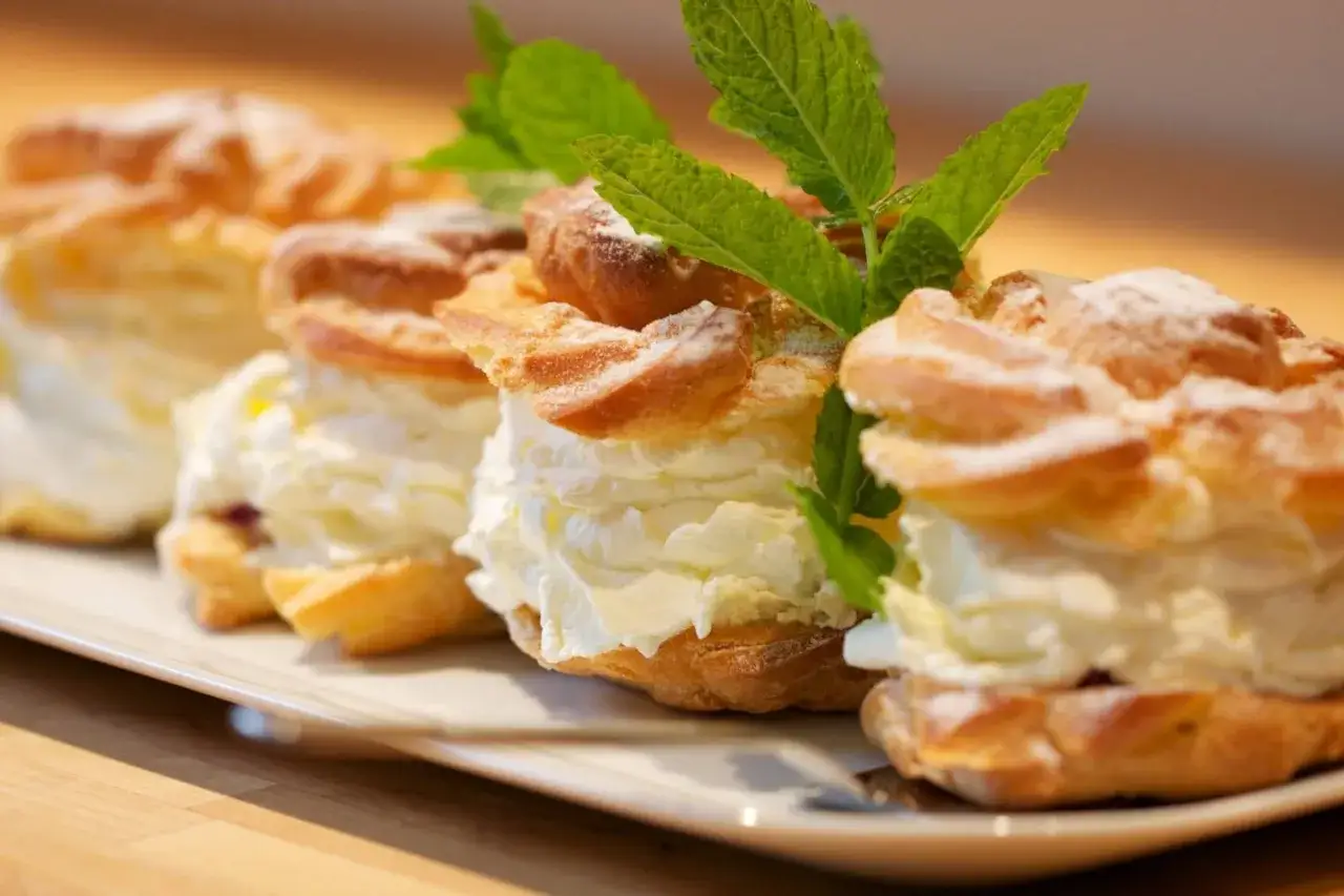 Eklery z czekoladą i profiteroles, puszyste ciastka przekładane kremem, ozdobione miętą i posypane cukrem pudrem.