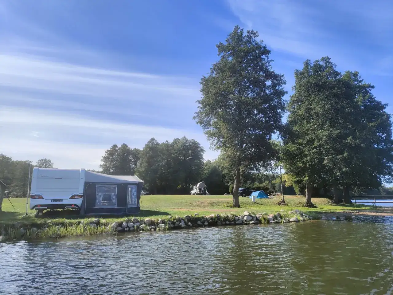 Przyczepa kempingowa i namiot stoją nad jeziorem, gotowe na wakacje pod namiotem.