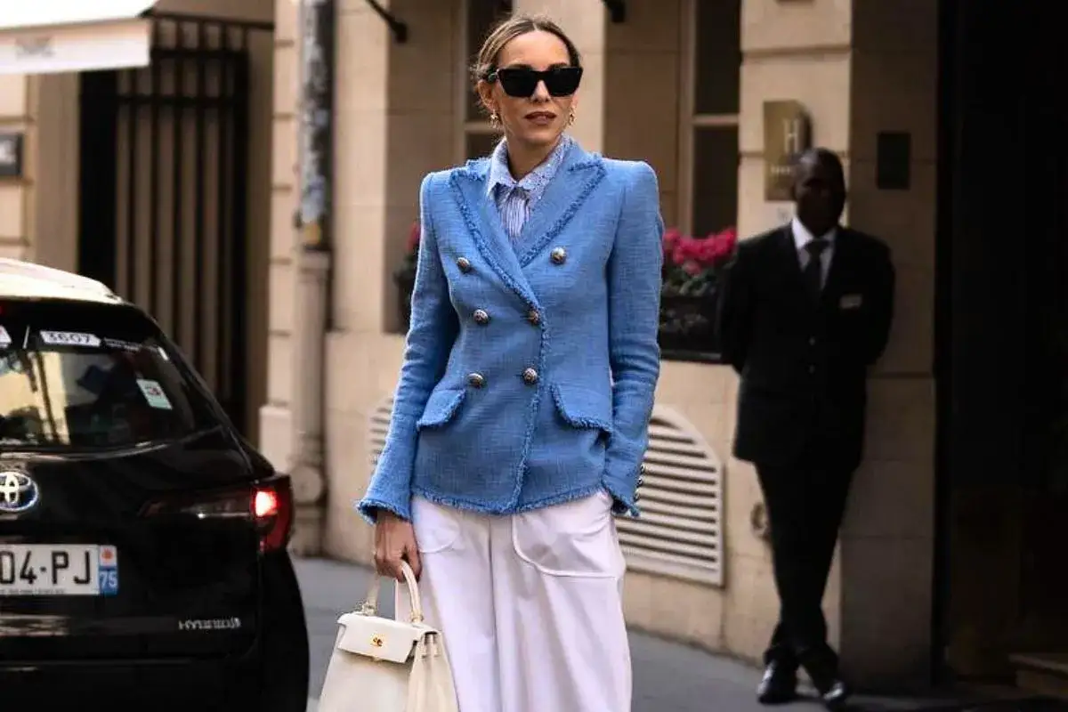 Elegancka kobieta po czterdziestce w niebieskiej marynarce i białych spodniach, z białą torebką. Idealna moda dla 40 latki.