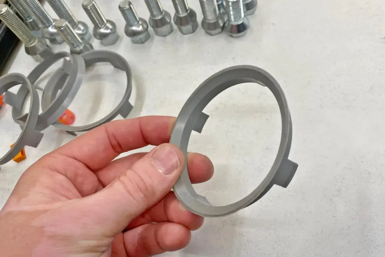 Dłoń trzyma pierścień centrujący. W tle widać śruby i inne pierścienie, sugerujące problem z za małym otworem centrującym felgi.
