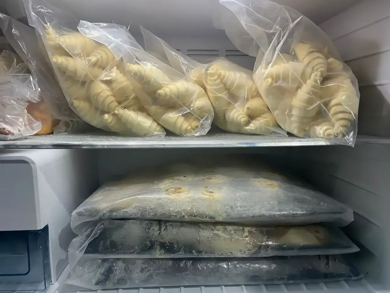 W zamrażarce piętrzą się torby z ciastami: na górze surowe rogaliki, na dole płaskie, zamrożone wypieki. Widać, jakie ciasta można mrozić.