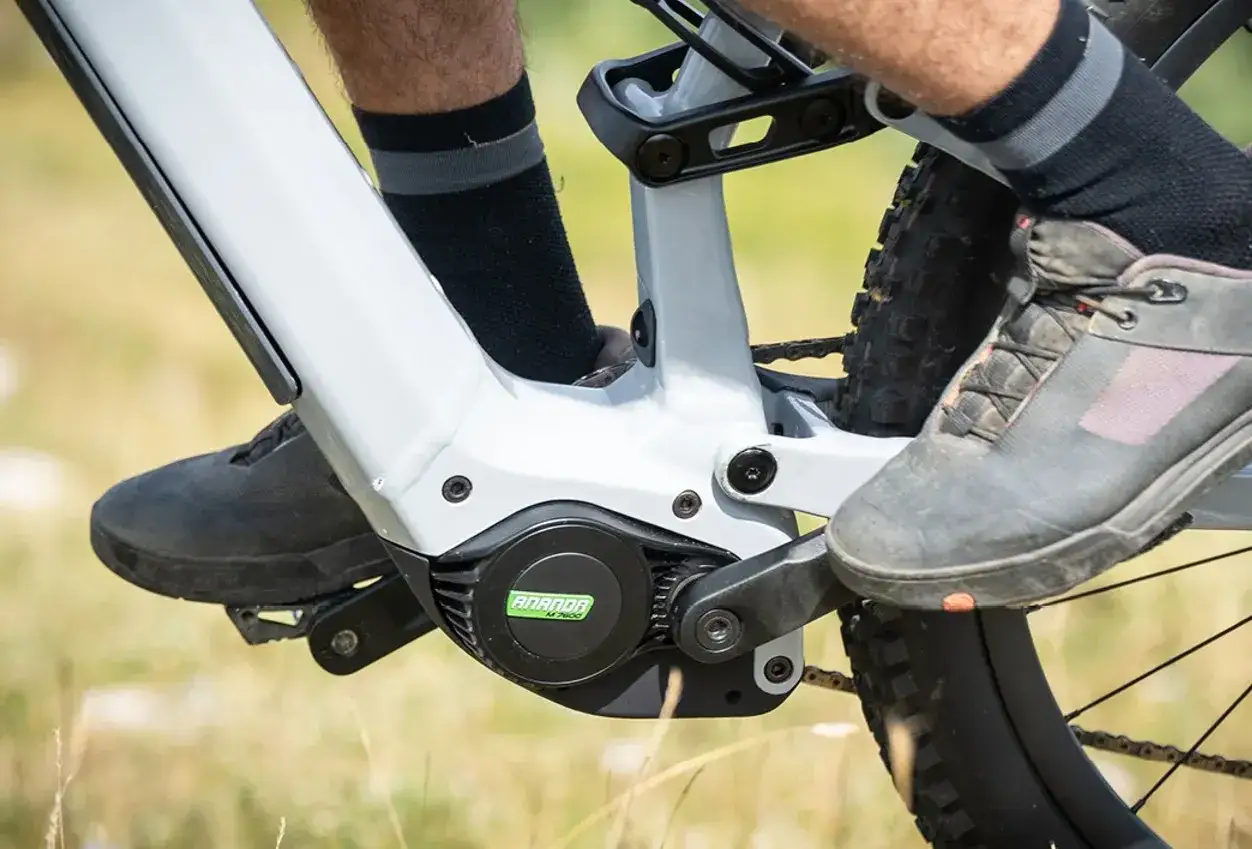 Jaki silnik do roweru elektrycznego? Widok na silnik Ananda M760 w rowerze elektrycznym, z nogami rowerzysty w butach i skarpetkach.