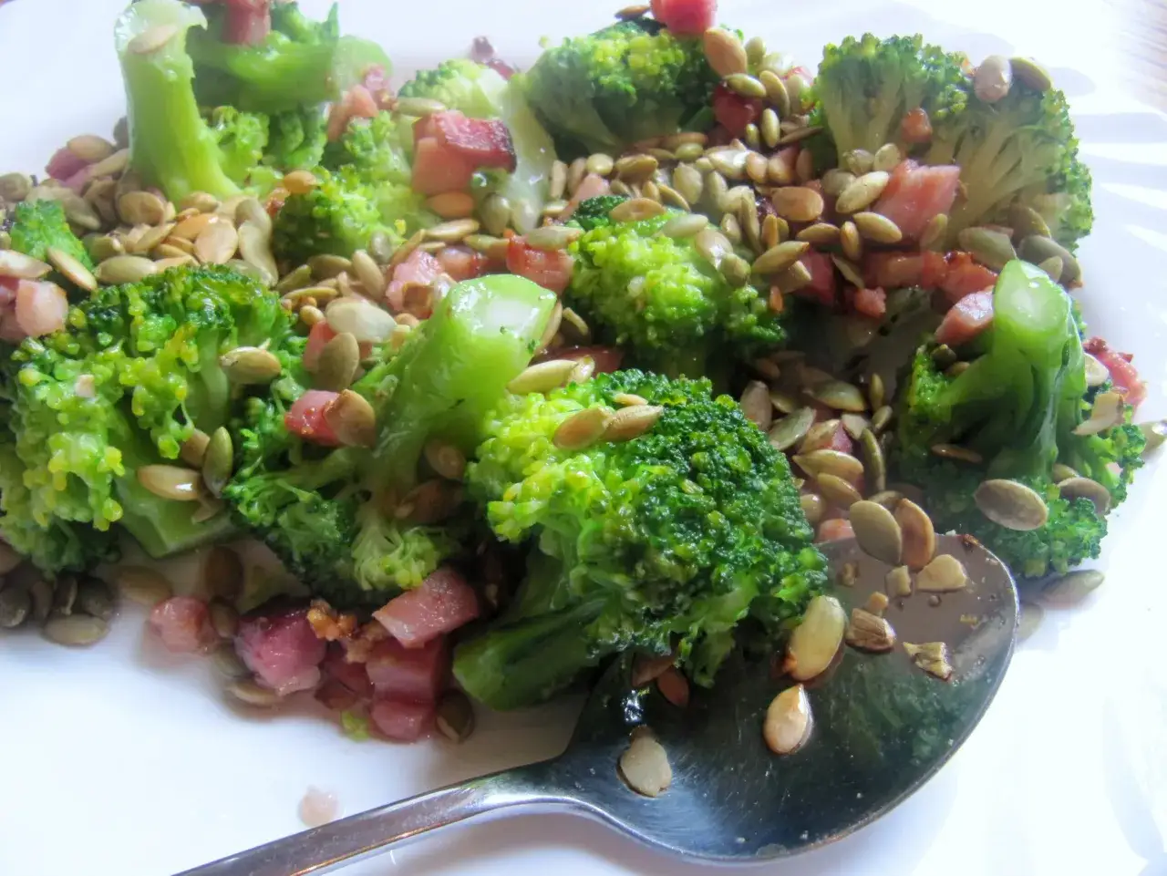 Sałatka z brokuła i boczku, posypana pestkami dyni. Apetyczna i kolorowa potrawa na talerzu.