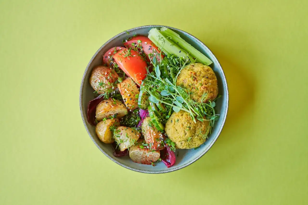 Falafel kontra kotlety sojowe: miska pełna smaków z pieczonymi ziemniakami, pomidorami, ogórkiem i kiełkami.
