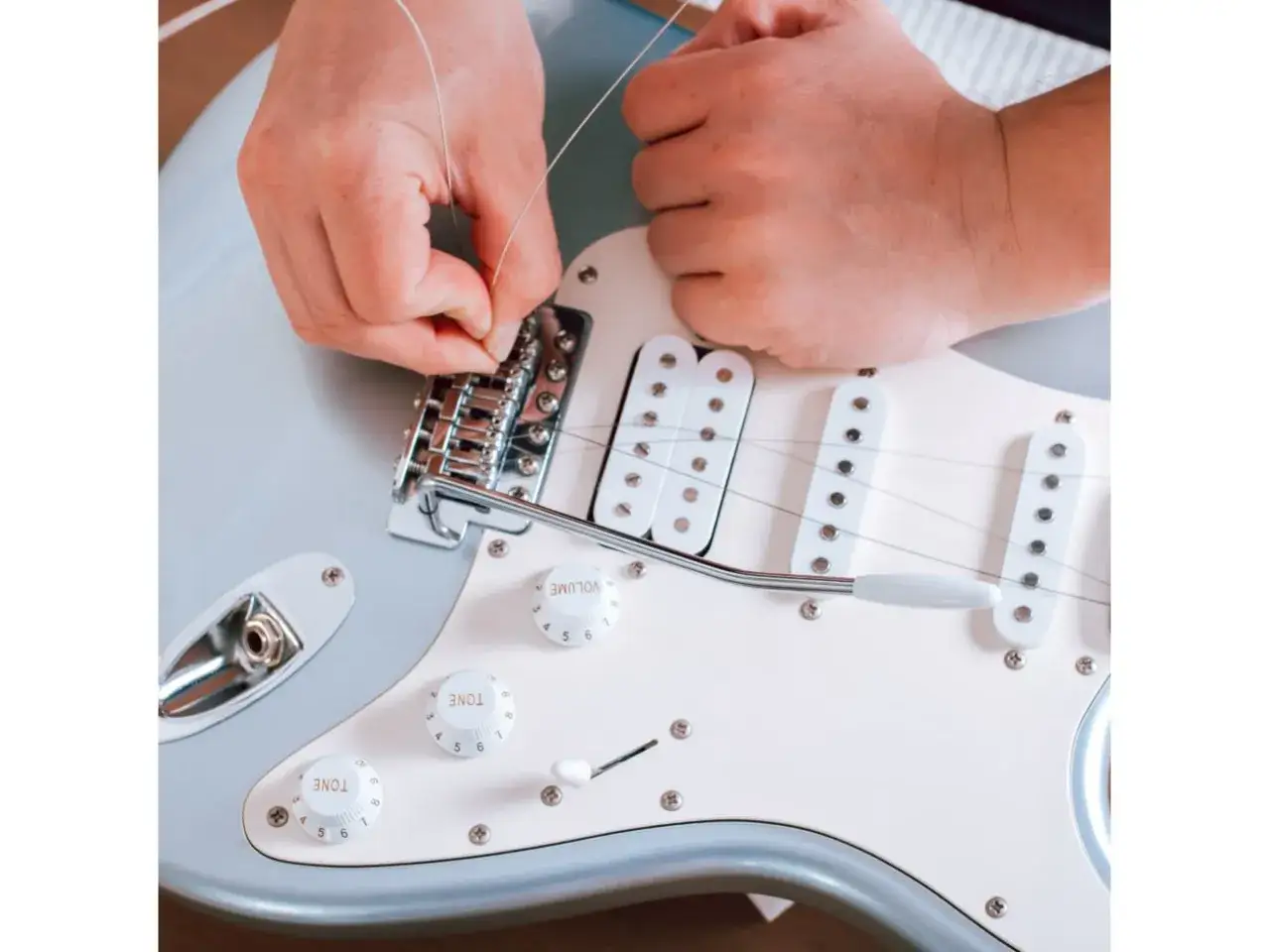 Dłonie montują nową strunę do mostka gitary elektrycznej. Praktyczny poradnik, jak zmienić struny w gitarze elektrycznej.