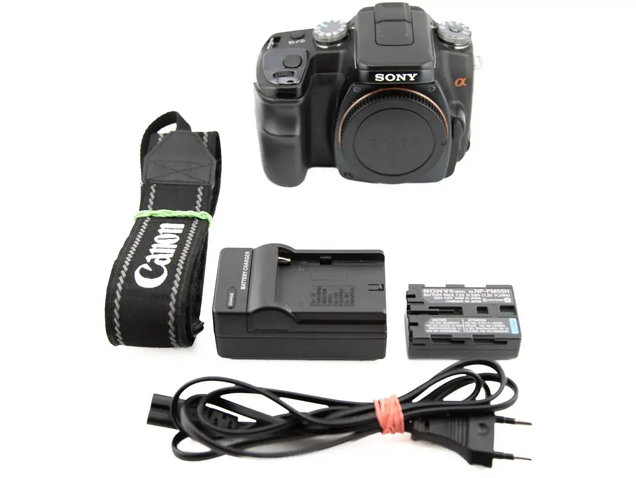 Aparat Sony Alpha A100 z paskiem Canon, ładowarką i baterią.