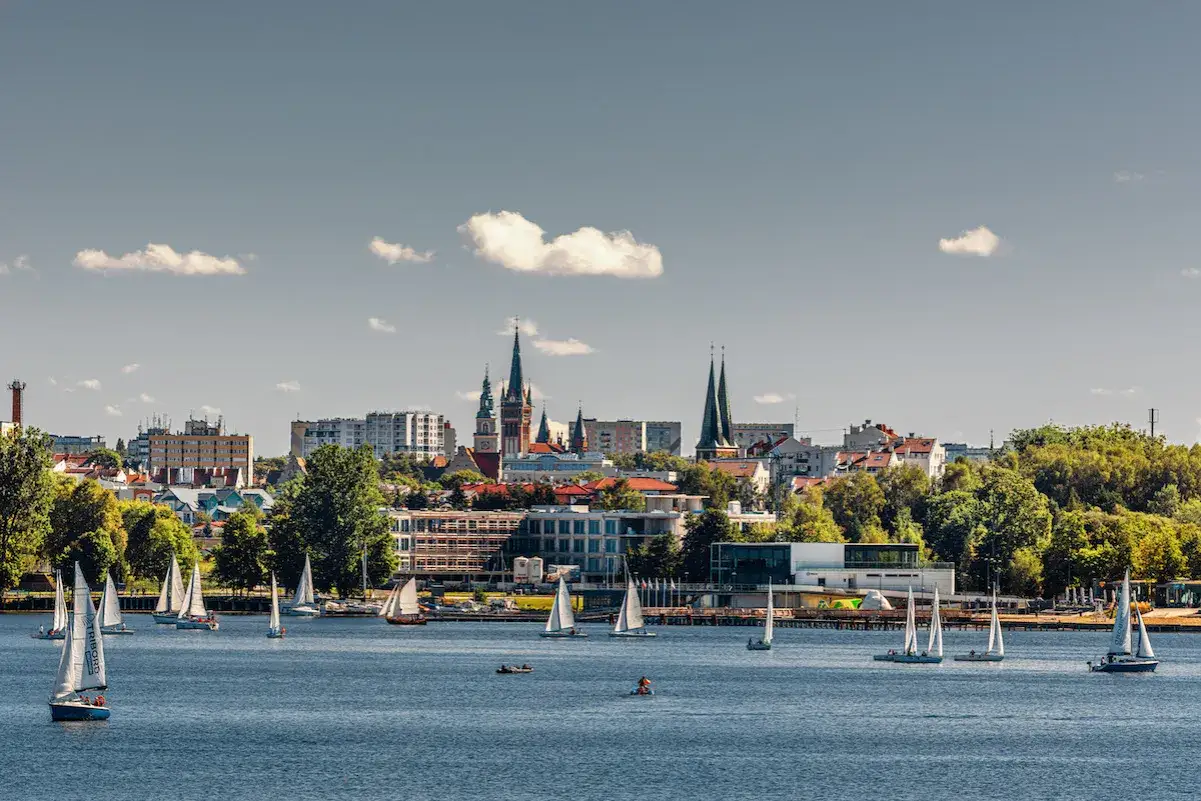 Żeglujące łodzie na jeziorze przed Olsztynem. Warto zobaczyć w Olsztynie piękną panoramę miasta z wieżami kościołów.