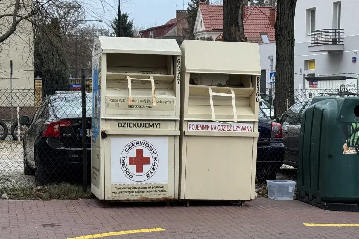 Dwa kontenery na ubrania stoją obok siebie. Jeden z nich ma logo Polskiego Czerwonego Krzyża.