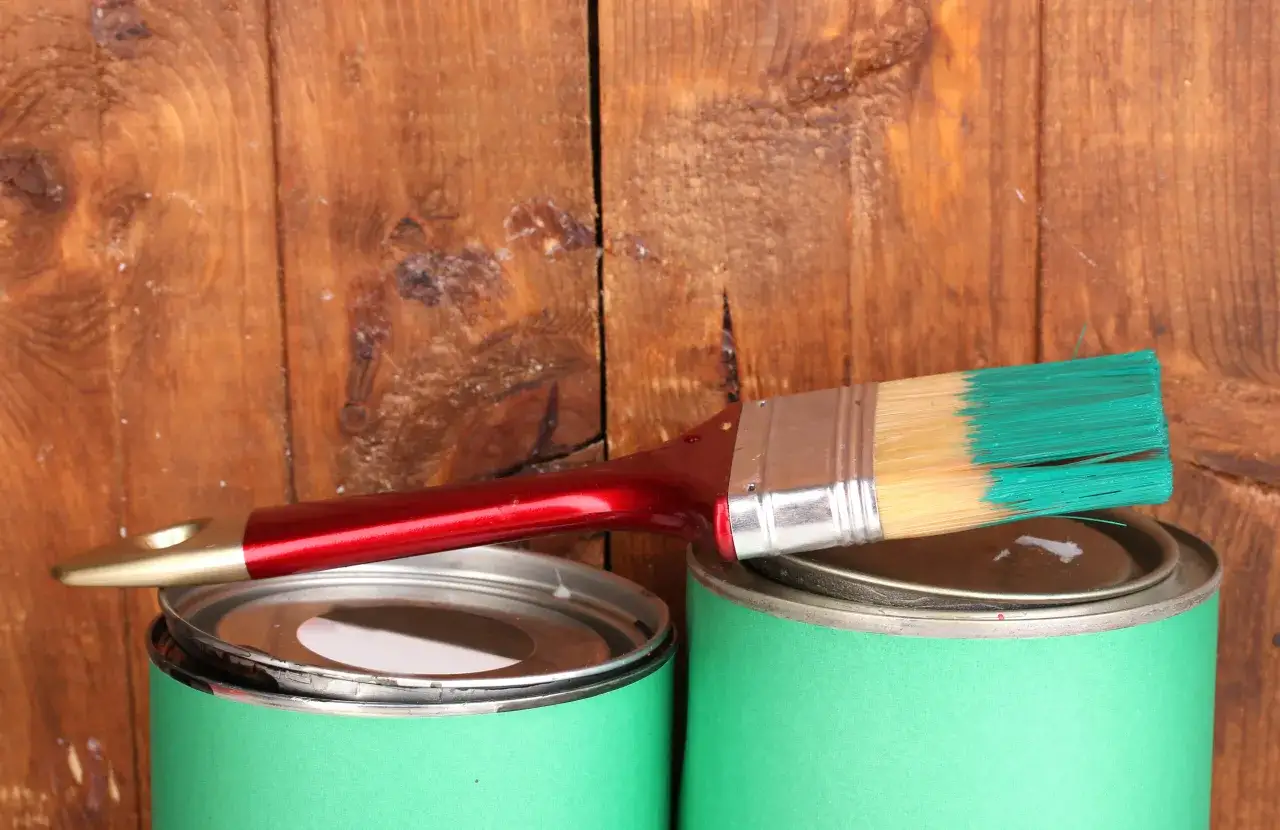 Pędzel z zieloną farbą na zielonych puszkach, gotowy do malowania ogrodzenia. Jaka farba na rdzę ogrodzenie?