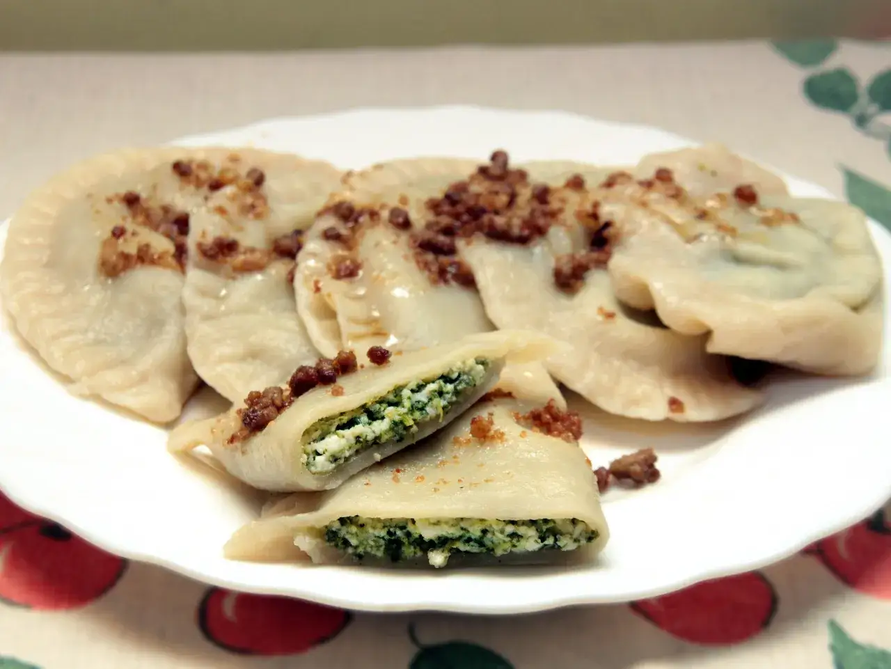 Pyszne pierogi ze szpinakiem i serem, posypane skwarkami, na białym talerzu.