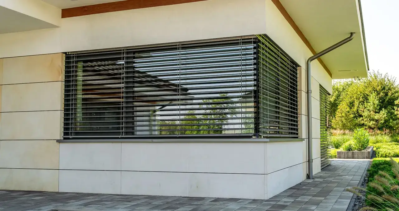 Nowoczesny dom z kamienną elewacją i dużymi oknami, na których zamontowano żaluzje zewnętrzne elektryczne.