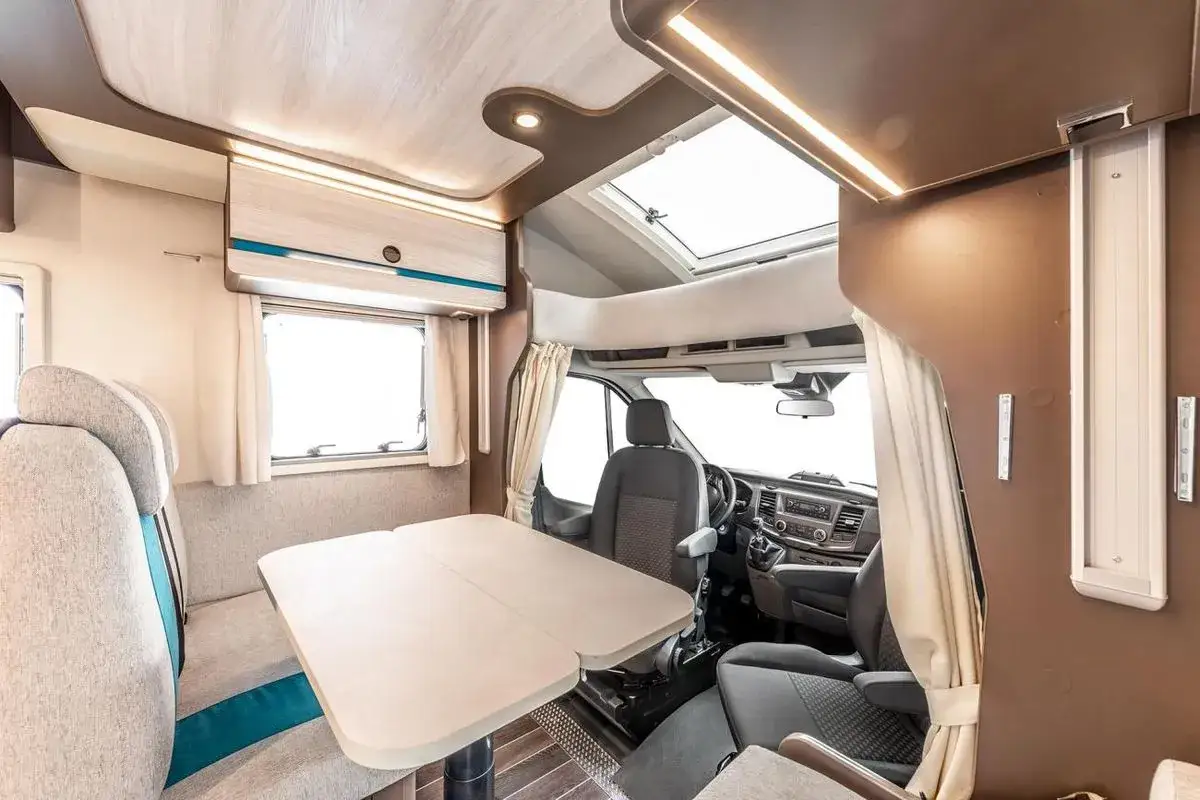 Wnętrze kampera tanio: rozkładany st&oacute;ł, wygodne siedzenia, kuchnia i łazienka. Idealny na podr&oacute;że!