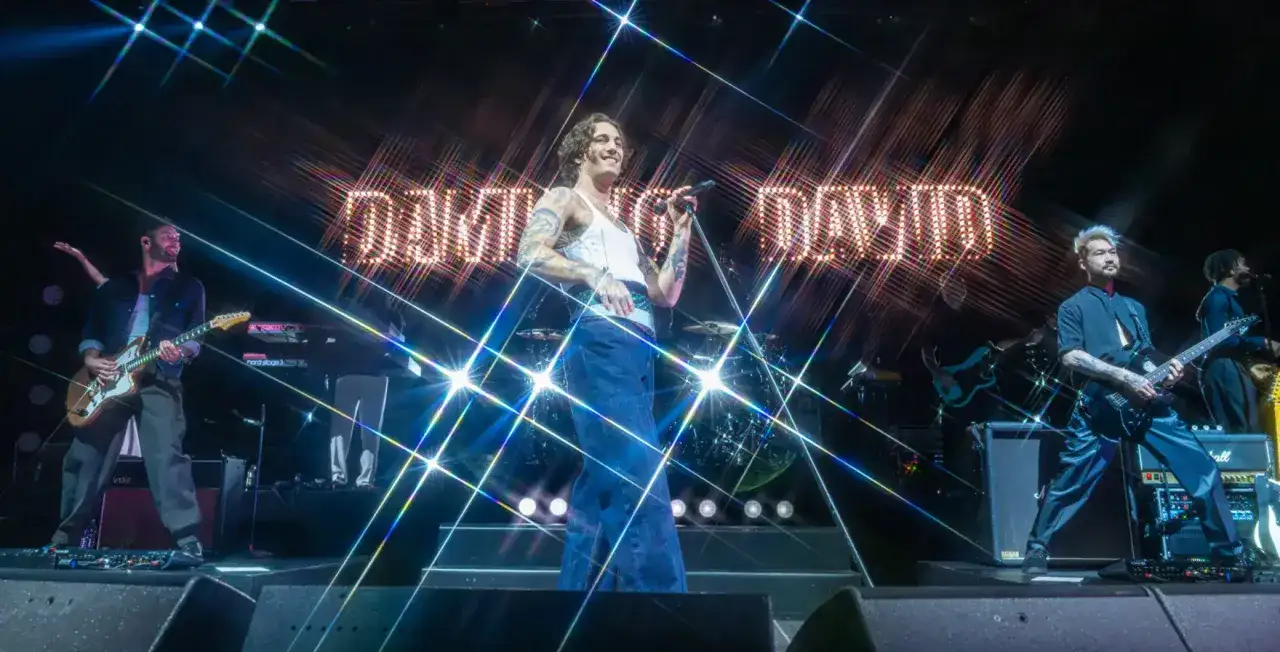 Damiano David na scenie, w otoczeniu zespołu, wykonuje swoje utwory. Światła i błyski podkreślają energię występu.