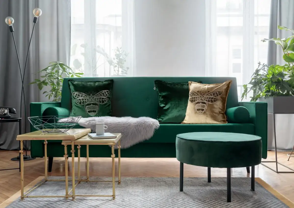 Elegancka zielona kanapa z poduszkami w pszczoły. Szare zasłony i złote stoliki tworzą przytulną atmosferę. Jakie zasłony do zielonej kanapy? Te szare pasują idealnie!