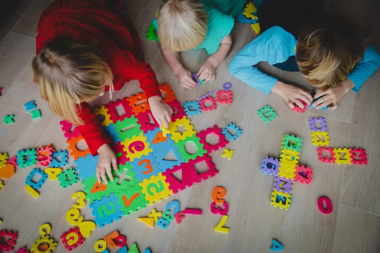 Dzieci bawią się kolorowymi piankowymi puzzlami z literami i cyframi, tworząc ciekawe wzory. To świetne gry dla dzieci 6 lat do nauki przez zabawę.