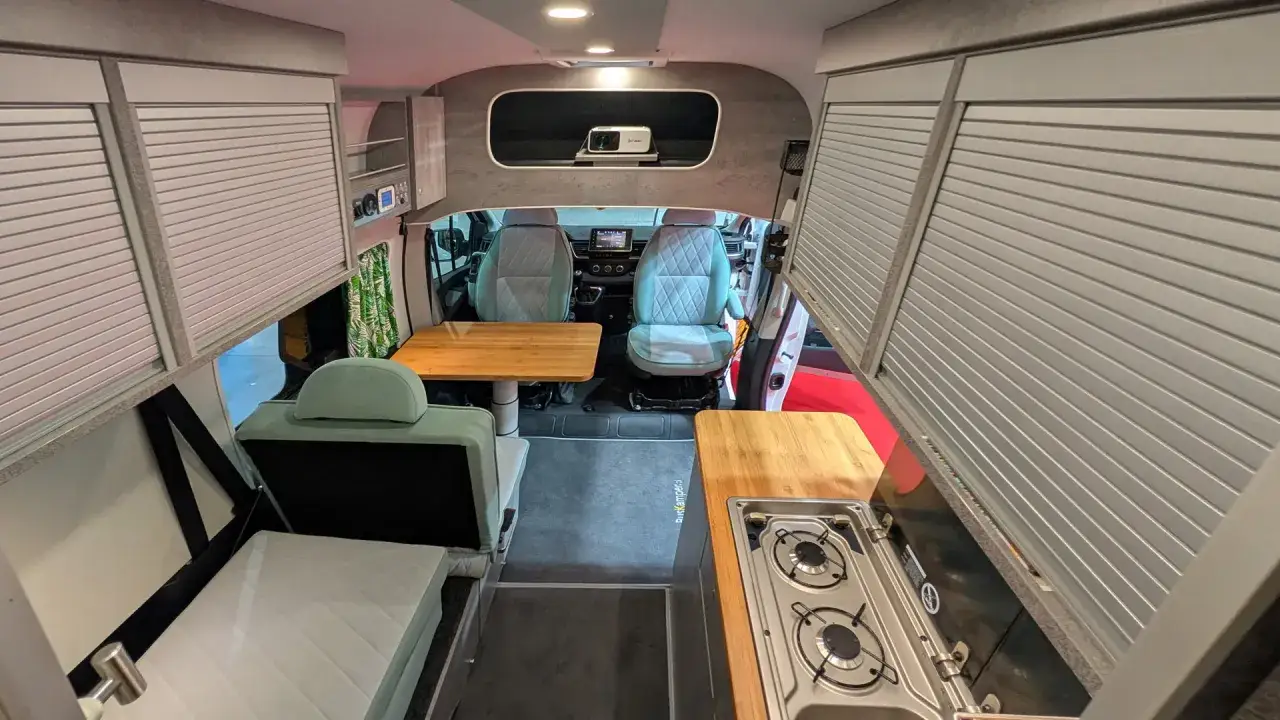 Wnętrze nowoczesnego busa kampera z wygodnymi siedzeniami, aneksem kuchennym i rozkładanym łóżkiem.