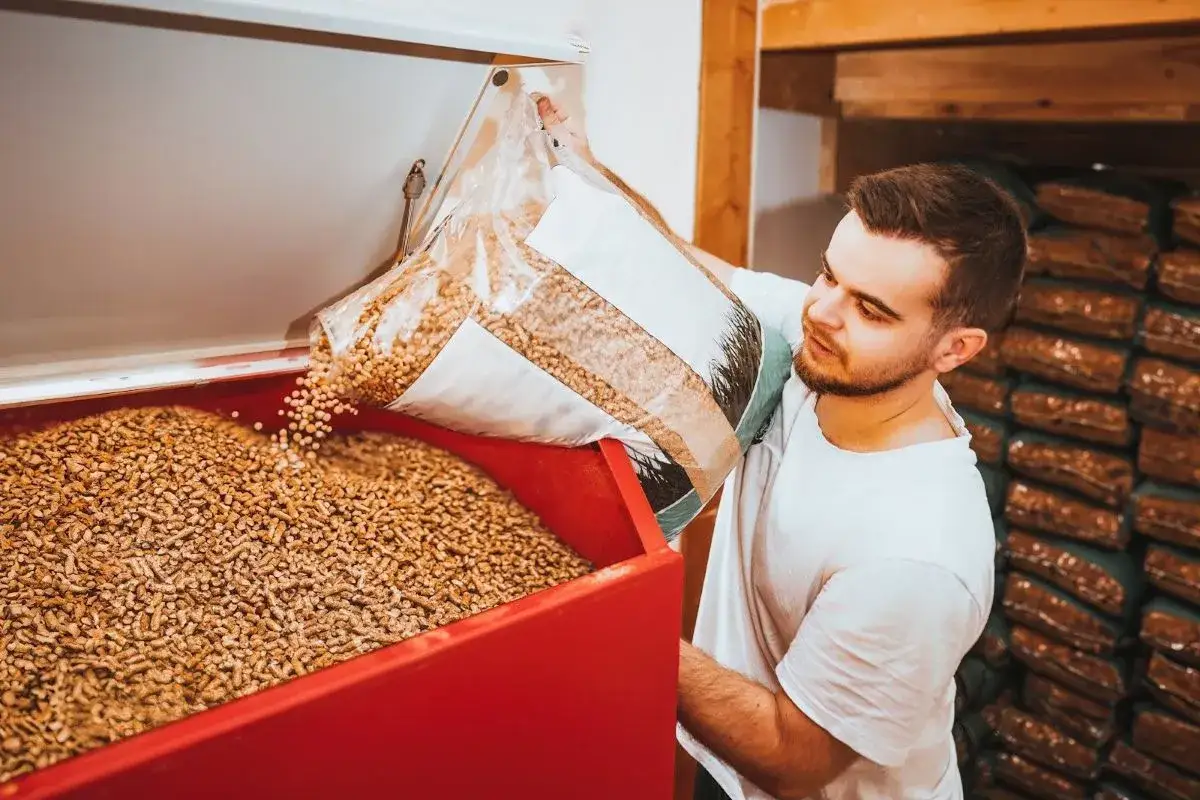 Mężczyzna wsypuje pellet do zasobnika, przygotowując się na zimę. Zastanawiasz się, ile pelletu potrzeba na zimę?