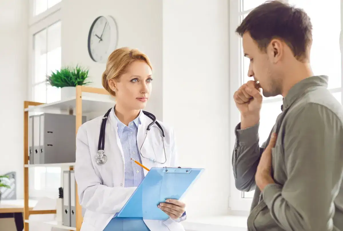 Lekarka z notatkami słucha pacjenta kaszlącego. Rozmowa o tym, ile dni do przodu można wystawić L4.