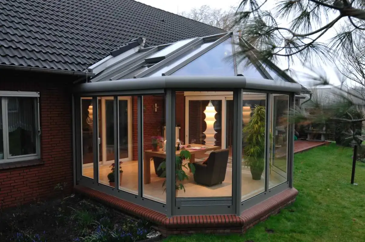 Nowoczesny ogród zimowy aranżacje: przeszklony salon z drewnianym stołem, fotelem i roślinami.