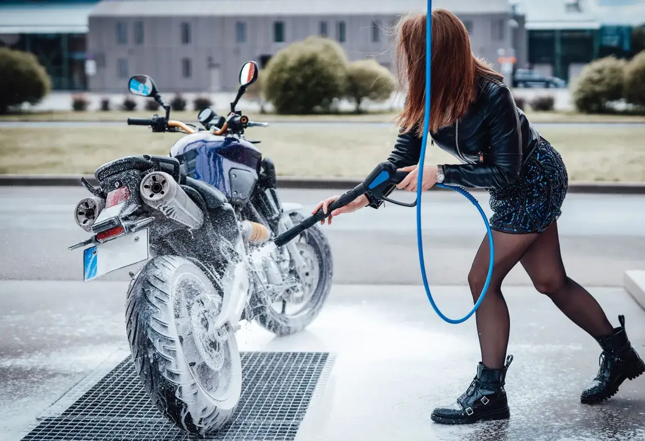 Kobieta myje motocykl na myjni. Czy można myć motocykl na myjni? Tak, jak widać na zdjęciu, jest to możliwe i skuteczne.