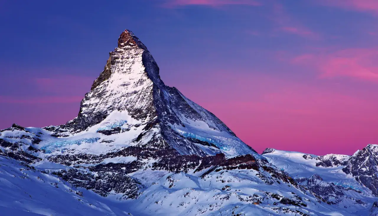 Szwajcaria g&oacute;ry gdzie jechać? Majestatyczny Matterhorn ośnieżony, z lodowcami, na tle purpurowego nieba. Idealne miejsce na zimowy wypad.
