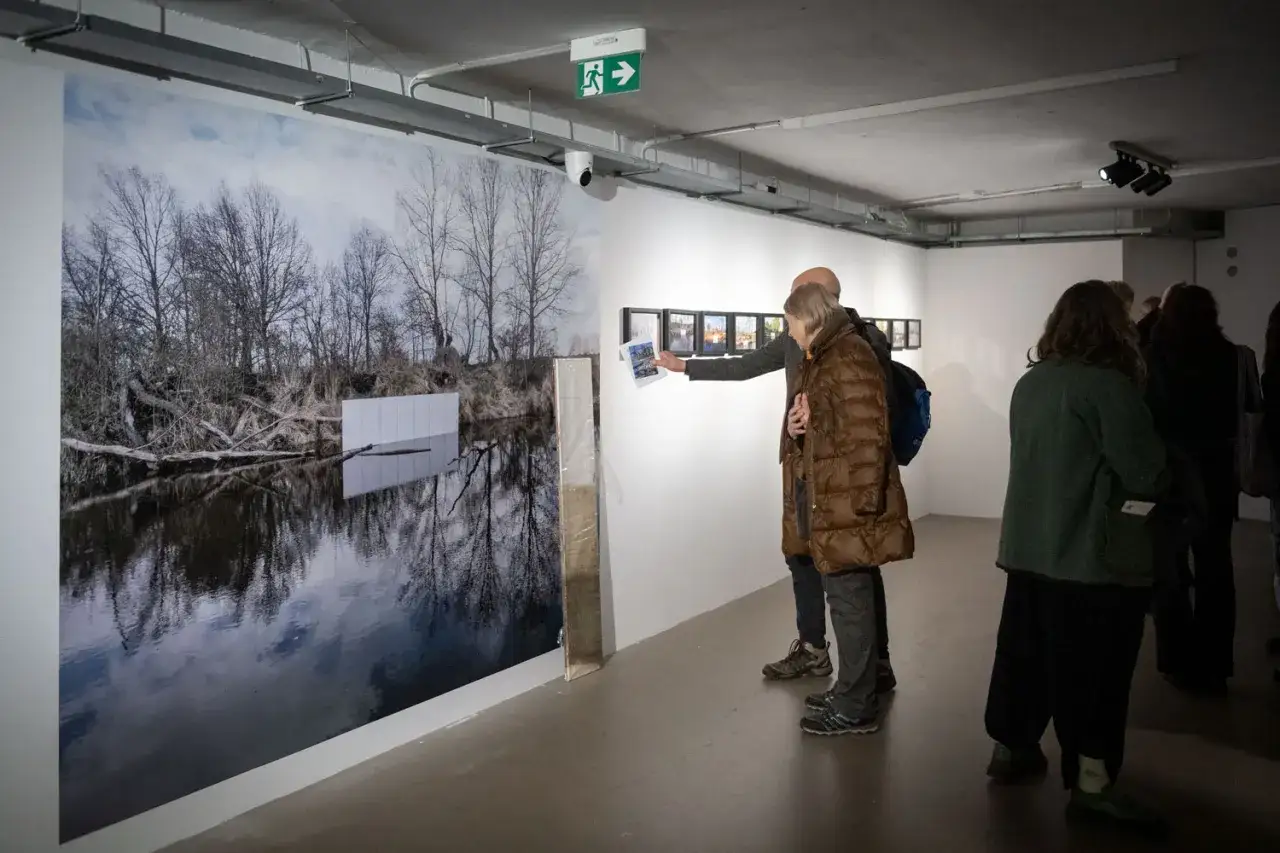 Wernisaż prac Piotra C. Kowalskiego. Ludzie oglądają jego instalację z zimowym krajobrazem i odbiciem w wodzie.