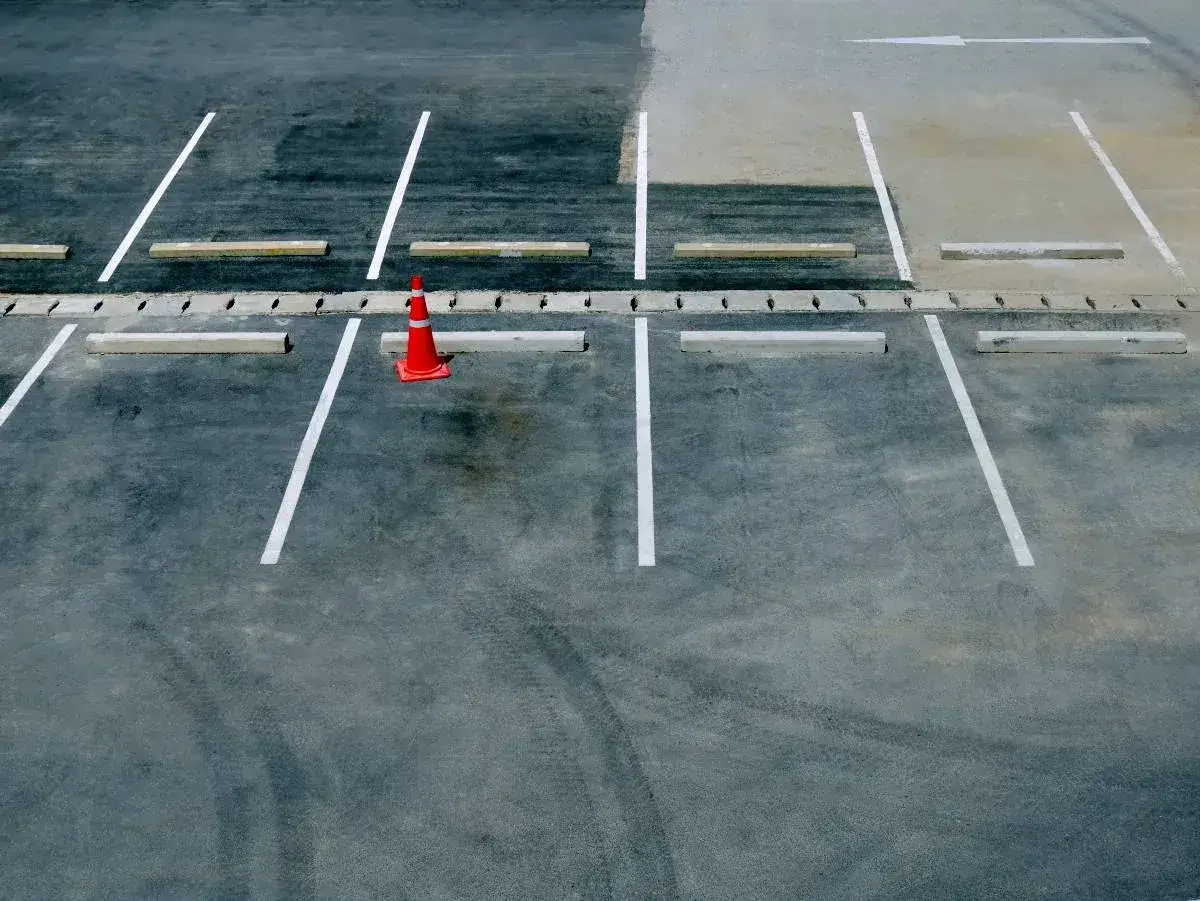 Pomarańczowy pachołek jako blokada na miejsce parkingowe. Puste miejsca parkingowe z białymi liniami i betonowymi ogranicznikami.