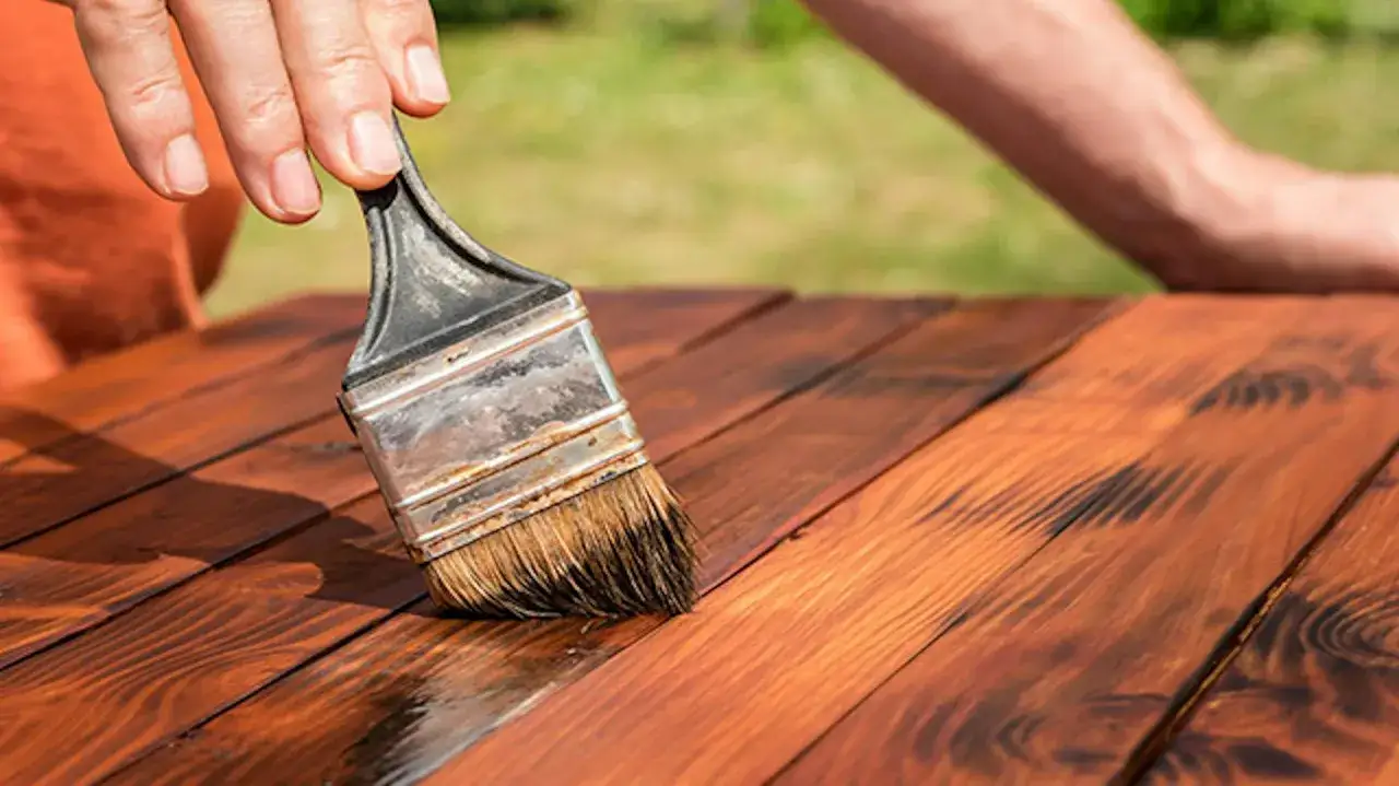 Nakładanie pędzlem impregnatu do drewna na zewnątrz na drewniany stół.