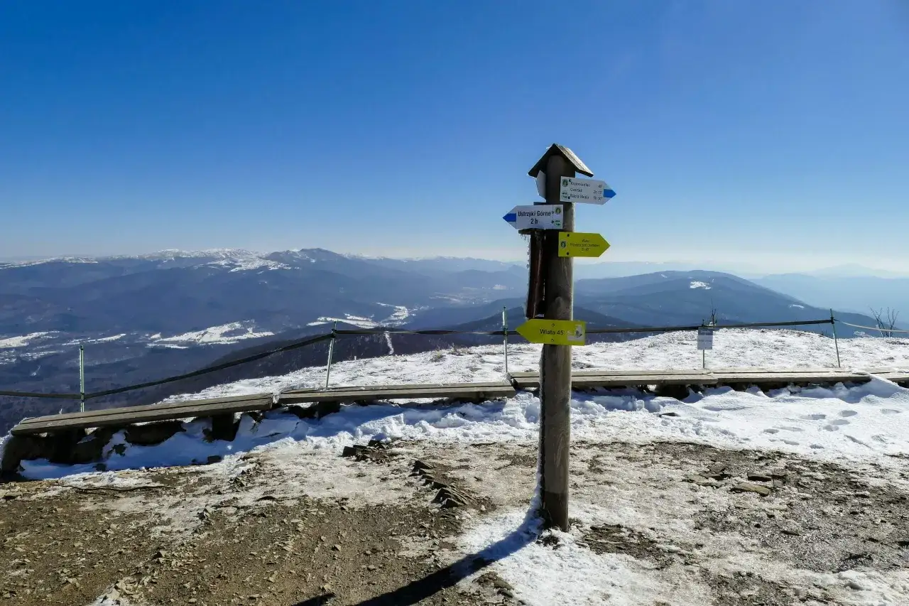 Zimowy krajobraz z drogowskazami w kierunku bac&oacute;wki pod Małą Rawką. W tle g&oacute;ry i błękitne niebo.