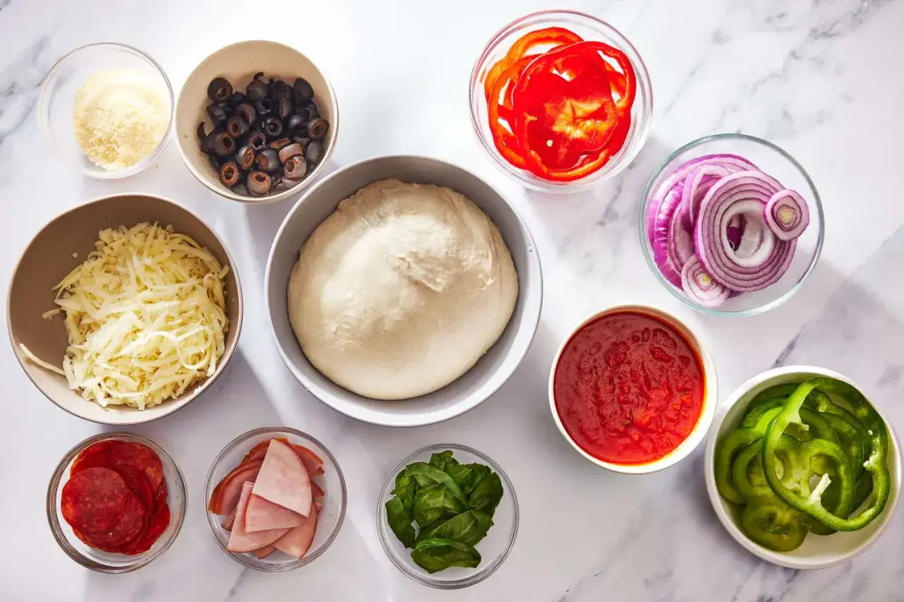 Ciasto na pizzę, sos, ser, salami, szynka, oliwki, papryka, cebula i bazylia &ndash; wszystkie te dodatki do pizzy czekają na swoją kolej.