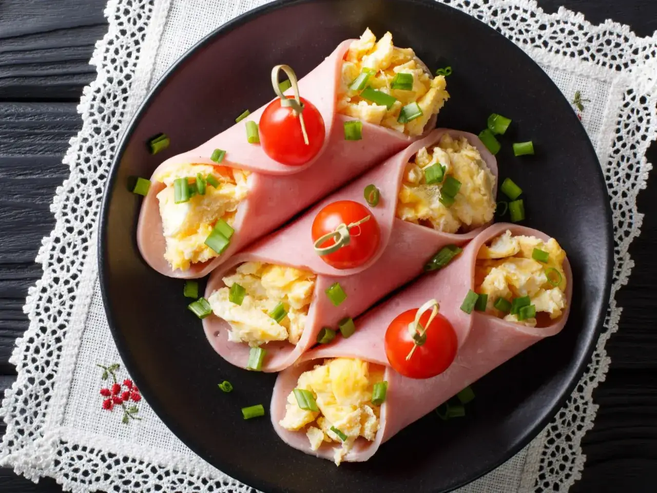 Roladki z szynki konserwowej z jajecznicą i szczypiorkiem, ozdobione pomidorkami koktajlowymi. Pyszna przekąska na śniadanie.