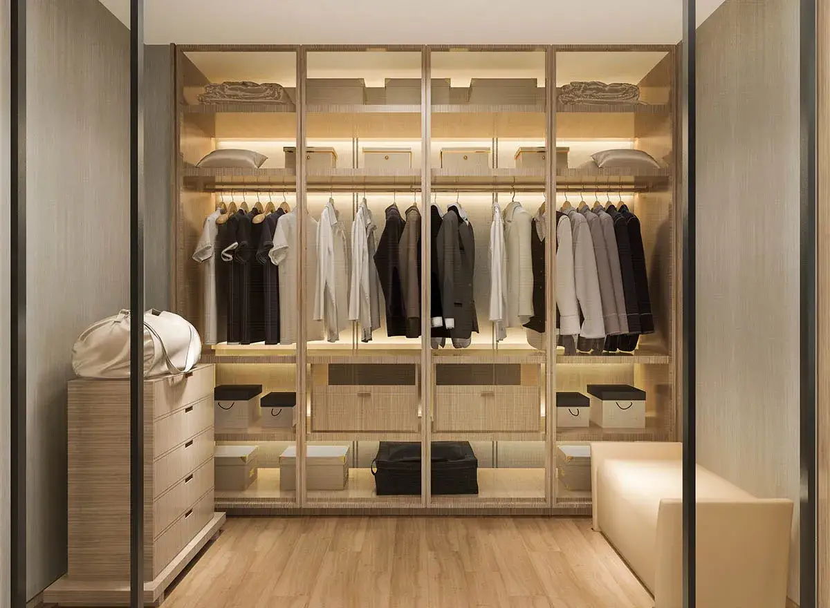 Nowoczesna garderoba ze skosem projekt. Wnętrze z wieszakami pełnymi ubrań, szufladami i pufą.