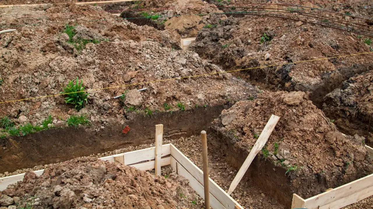 Wykonano wykop pod fundament. Widać ziemię, drewniane szalunki i zbrojenie.