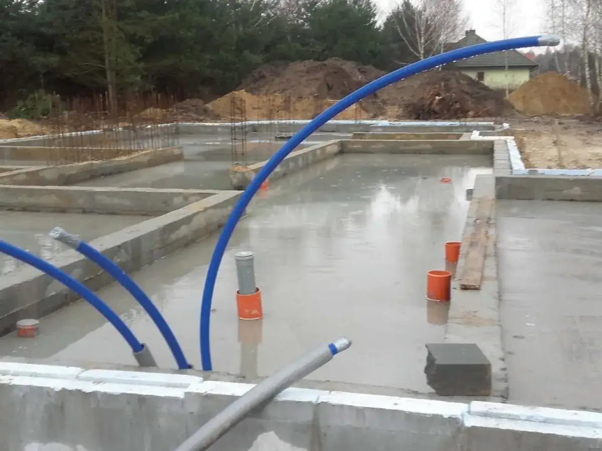 Samodzielne wykonanie przyłącza wodociągowego na budowie. Widać fundamenty, zbrojenia i niebieskie rury.