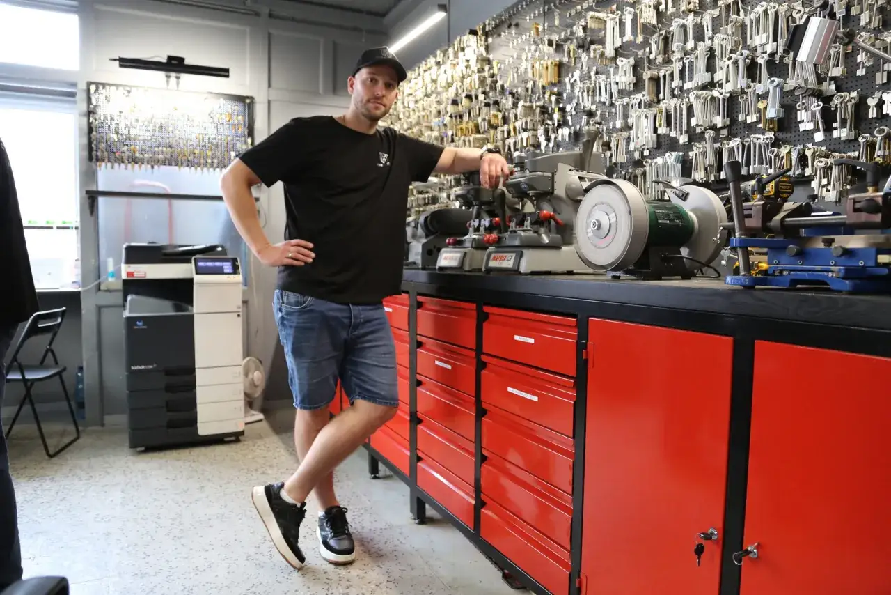 Mężczyzna w czapce stoi obok maszyn do dorabiania kluczy. Na ścianie wisi mnóstwo kluczy, więc wiesz, gdzie można dorobić klucz.