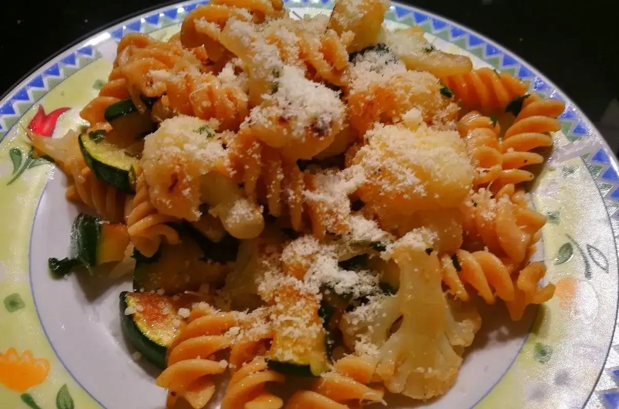 Pyszny makaron z kalafiorem i cukinią, posypany parmezanem. Danie wygląda apetycznie i zdrowo.