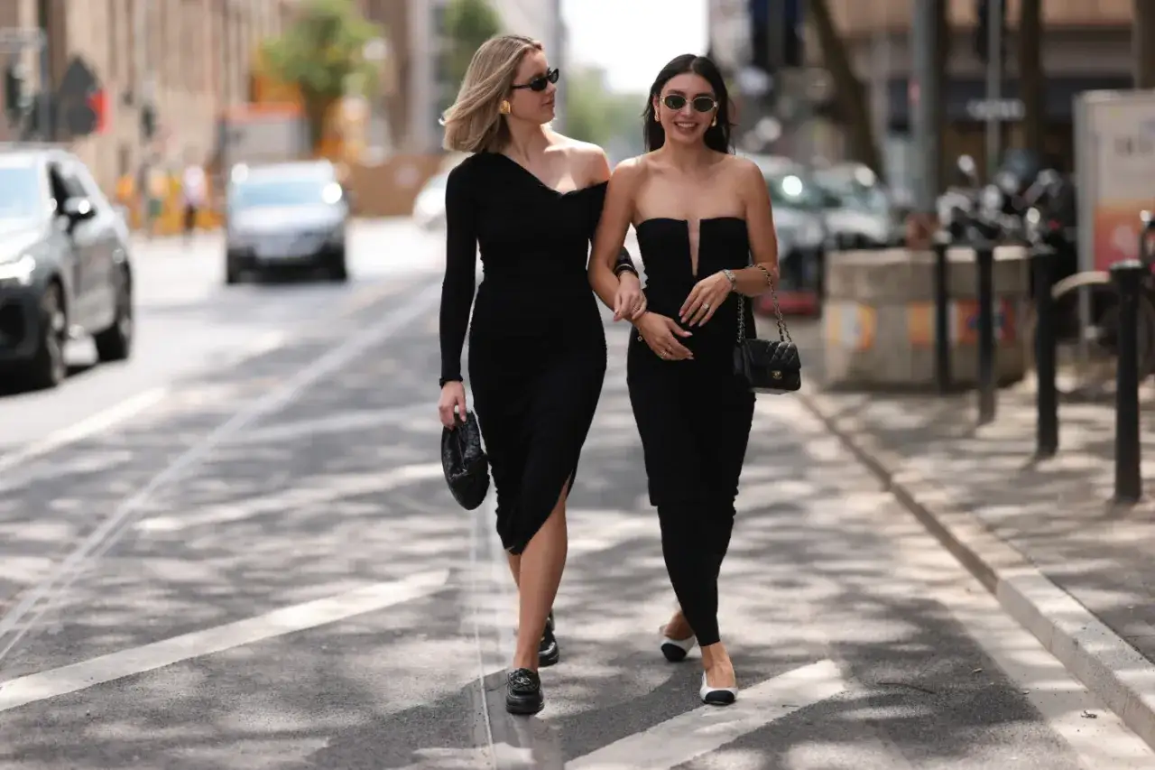 Dwie kobiety w czarnych sukienkach idą ulicą. Jedna ma czarne mokasyny, druga biało-czarne baleriny. Idealne buty do eleganckiej sukienki?