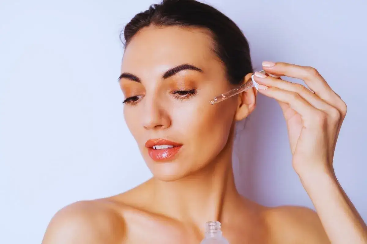 Kwas migdałowy na co? Kobieta aplikuje serum z kwasem migdałowym na twarz, by poprawić jej wygląd.