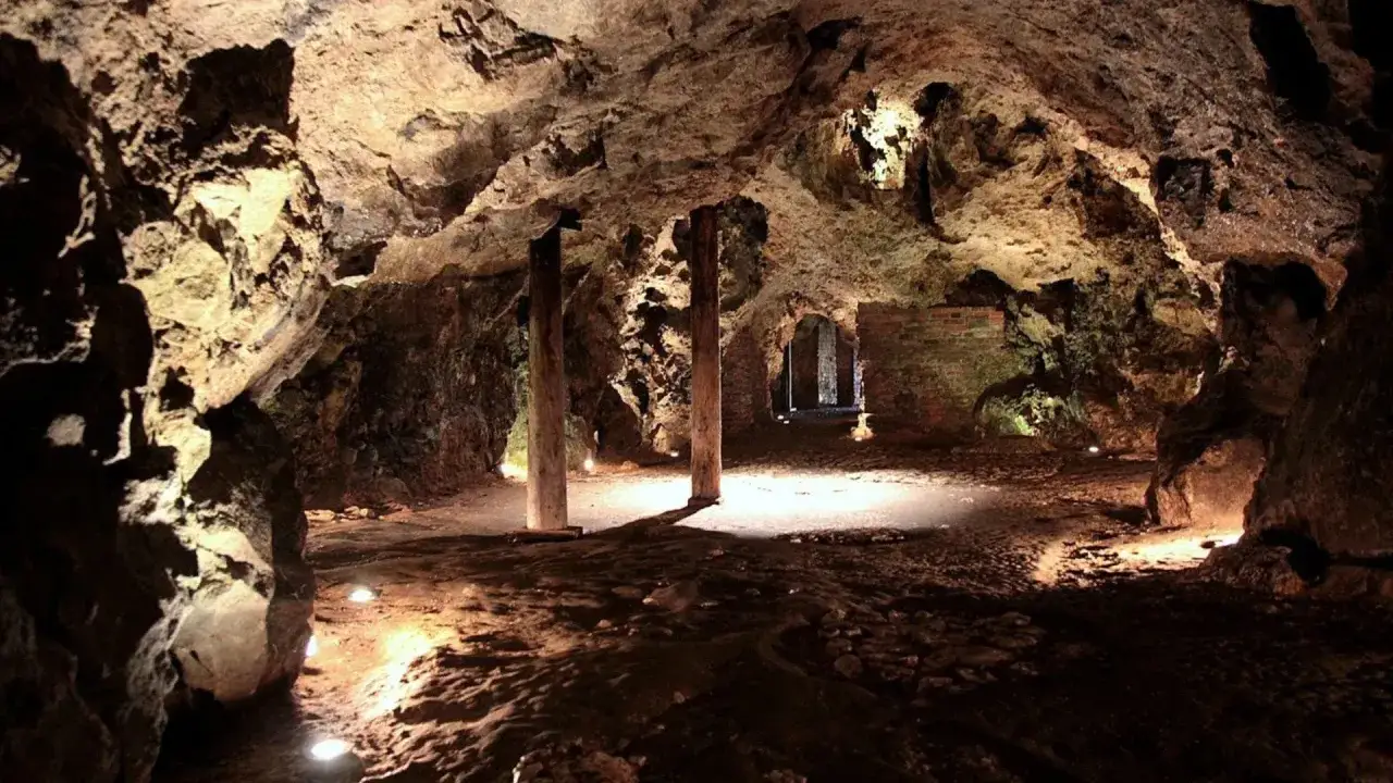 Wnętrze oświetlonej jaskini z kamiennymi ścianami i drewnianymi słupami. To jedna z najpiękniejszych jaskiń w Polsce, zachwycająca swym naturalnym pięknem.