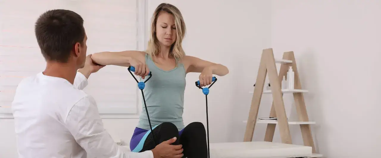 Fizjoterapeuta pomaga pacjentce z twardą piersią po radioterapii w ćwiczeniach z gumą oporową.