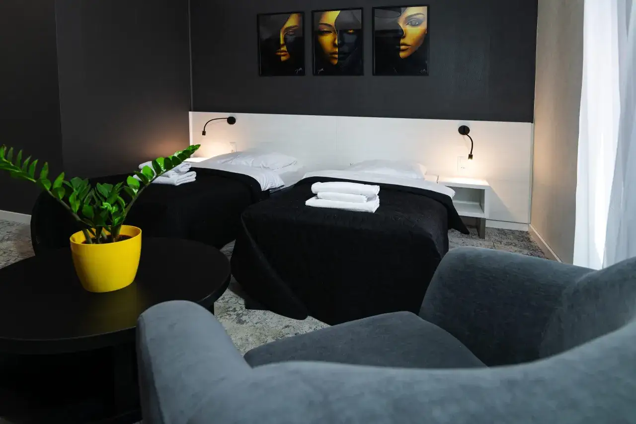 Nowoczesny pokój hotelowy z dwoma łóżkami, czarnymi narzutami i białymi poszewkami. Na ścianie trzy obrazy z twarzami. Dowiedz się, ile trwa doba hotelowa.