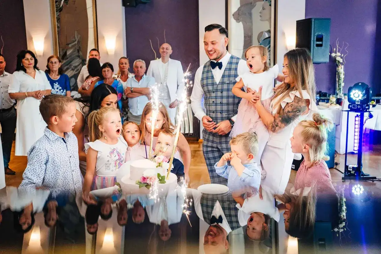 Rodzina świętuje chrzciny dziecka. Dzieci z zaciekawieniem patrzą na tort ze świecami.