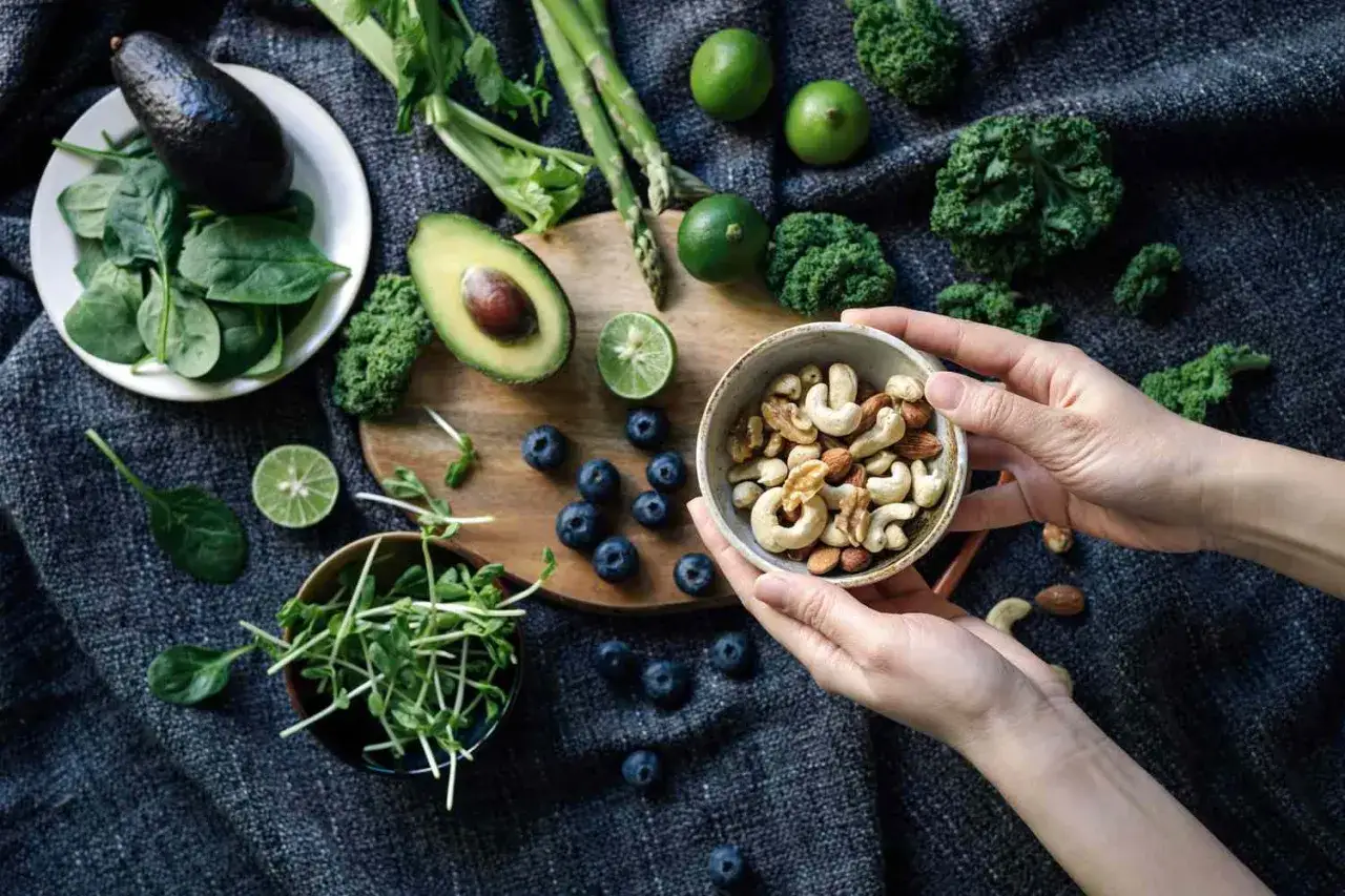 Ręce trzymają miseczkę orzech&oacute;w, obok awokado, szpinak, bor&oacute;wki i kiełki &ndash; naturalne produkty bogate w magnez i potas.