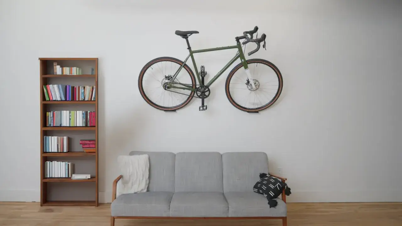 Zielony rower zawieszony na ścianie nad szarą kanapą. Obok regał z książkami. Oto jak powiesić rower na ścianie, by zaoszczędzić miejsce.