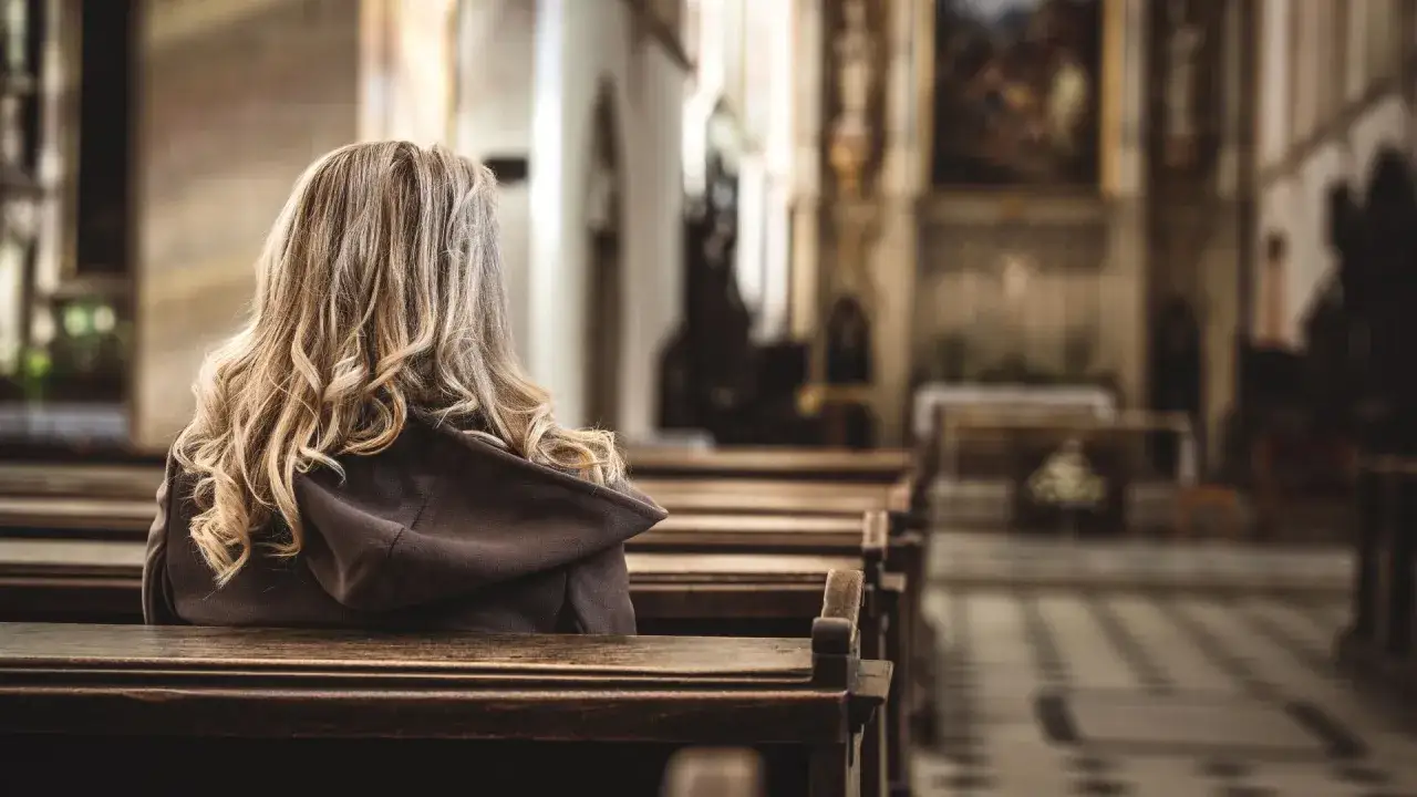 Kobieta w kościele, siedząca w ławce. Obraz symbolizuje praktyki religijne, zgodne z badaniem CBOS.