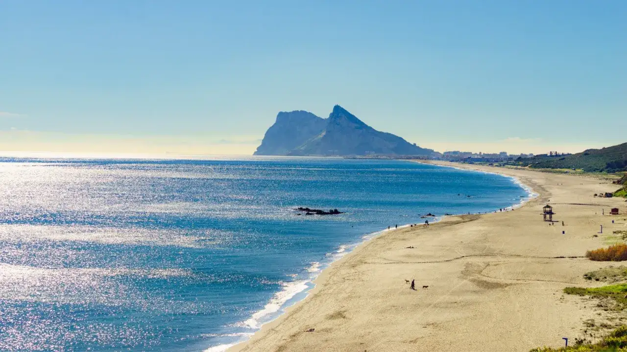 Słoneczna plaża z widokiem na Gibraltar. Błękitne, błyszczące morze zachęca do kąpieli, zastanawiając, które morze jest najcieplejsze.