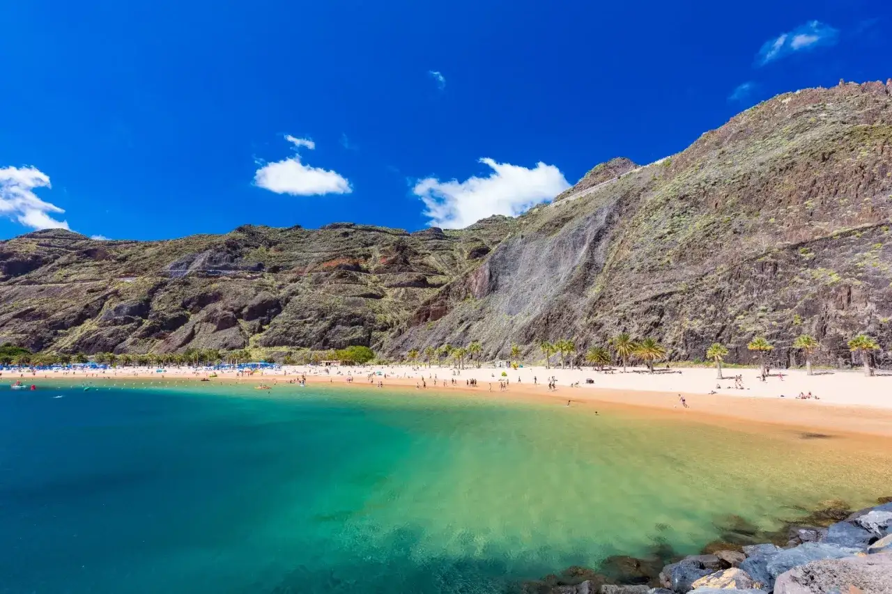 Idealne miejsce, gdzie na wakacje w czerwcu: piaszczysta plaża, turkusowa woda i skaliste g&oacute;ry w tle.