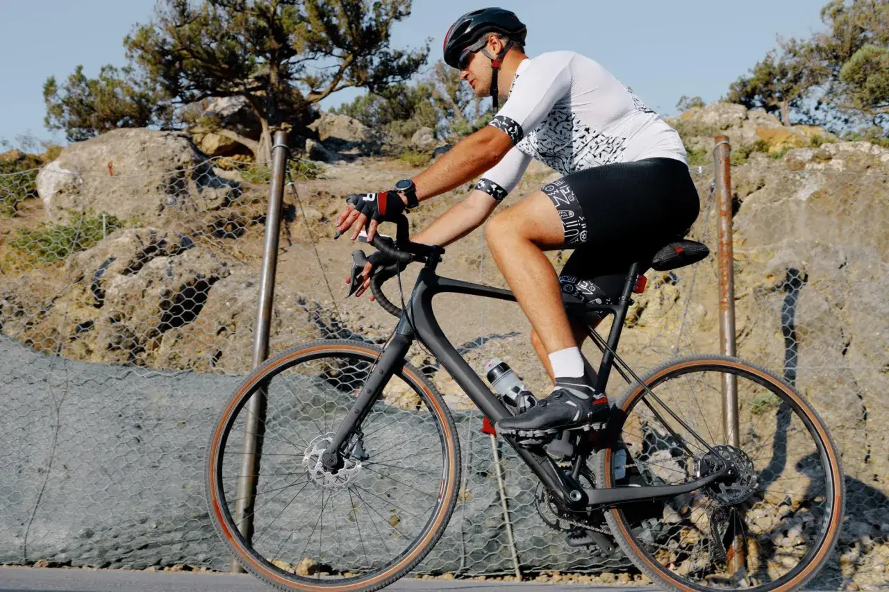Mężczyzna w kasku i sportowym stroju jedzie na rowerze typu gravel po kamienistej drodze.