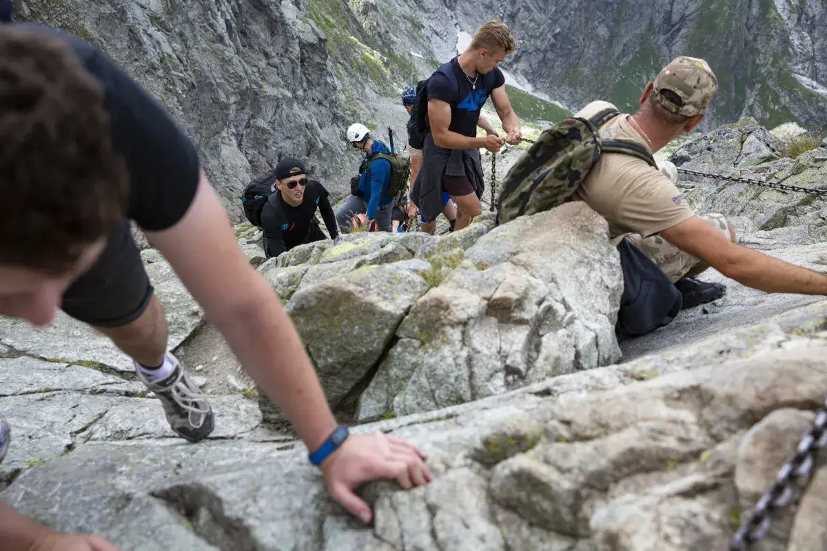 Grupa turyst&oacute;w wspina się po skalistym zboczu, korzystając z pomocy łańcuch&oacute;w.